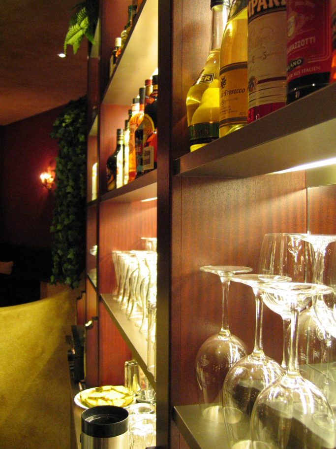 Beleuchtetes Regal mit Spirituosenflaschen hinter dem Tresen der Cocktailbar Mákaá